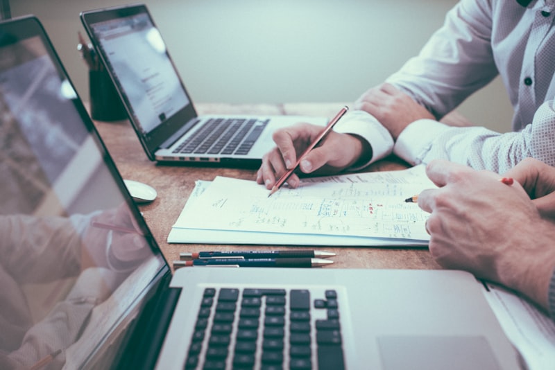 Hands reviewing a document beside laptops on a desk — suggested image — client to supply the final photograph