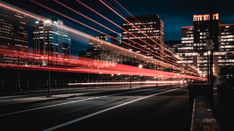 A long-exposure photograph of light trails along a road between office towers at night — suggested image — client to supply the final photograph